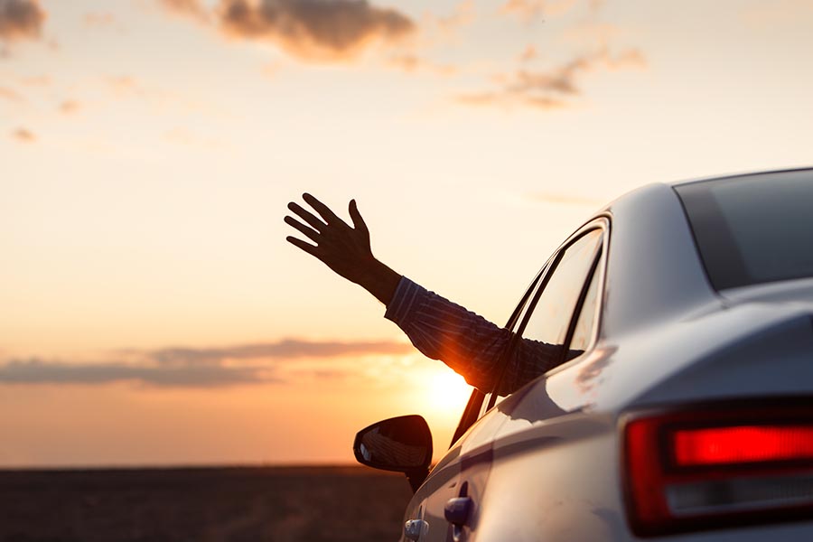 About Our Agency - Hand Waving Out of the Window of a Silver Car at Sunset