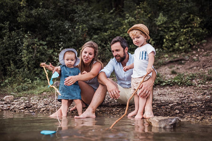 Personal Insurance - Family Playing at the Bank of a Small Lake, Poking at Rocks with Sticks