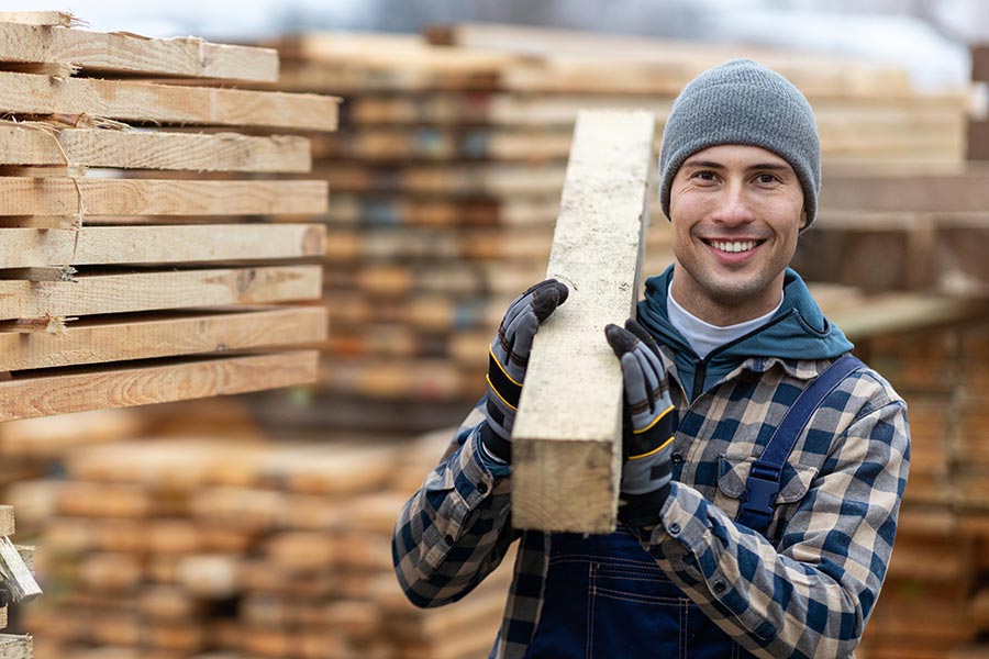 Business Insurance - Young Man Carrying Lumber in a Lumber Yard, Dressed for Cold Weather